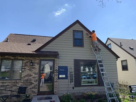 A person painting the exterior of a house in an orange shirt